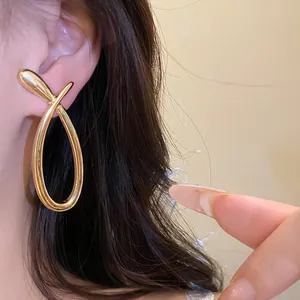 Detail showing elegant large golden crossover hollow earrings worn on a female model's ear