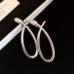 Macro close-up of minimalist silver cross hollow-out earrings on black textured background