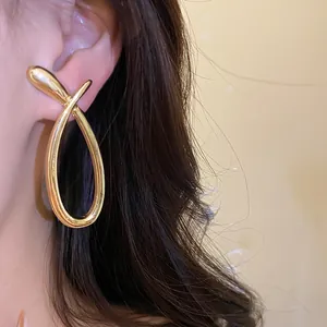 Close-up detail shot of a minimalist gold crossed hollow stud earring worn on a model's ear.