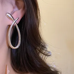 Close-up detail of polished silver crossover hollow earrings worn on a model's ear.