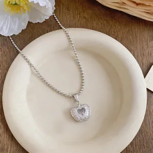 Dettaglio del pendente a forma di cuore-mela con zircone scintillante su catena a sfere