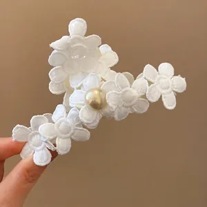 Elegant white fabric flower hair claw clip with central pearl detail on brown background
