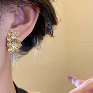 Close-up of vintage gold flower earrings with zircon stones worn on an ear.