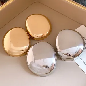 Close-up view of elegant gold and silver metallic glossy oval stud earrings on a tray