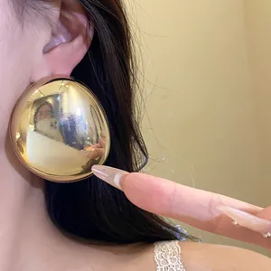 Close-up of large gold metallic oval stud earrings with high-shine mirror finish.
