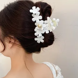 Detailed view of white fabric flower hair claw clip with elegant pearl on dark hair.