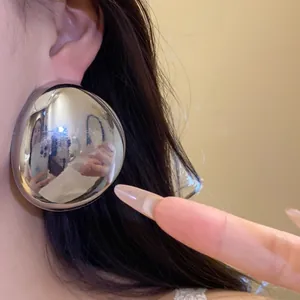 Close-up of large metallic oval stud earring with silver mirror finish worn on ear.