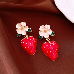 Close-up detail of enamel strawberry earrings with delicate white flower studs