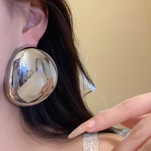 Close-up detail showing a large polished silver oval stud earring worn on an ear