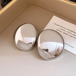 Close-up view of polished silver oval stud earrings on a cream jewelry tray.
