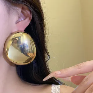 Close-up view of a glossy gold elliptical metal stud earring worn elegantly on a model's ear