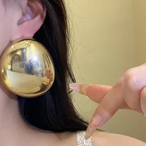 Close-up of a large glossy gold oval stud earring worn by a model for detail view