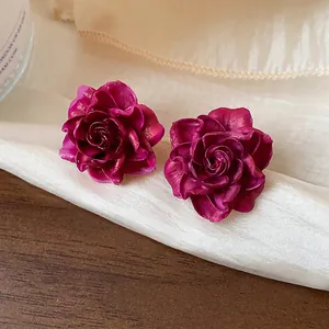 Detailed macro view of elegant magenta resin rose stud earrings on luxurious silk fabric