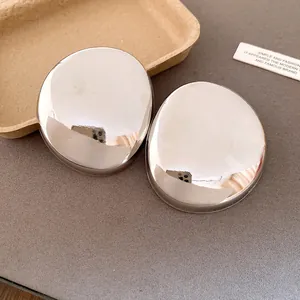 Close-up of oversized silver-tone oval stud earrings with high-polish metallic finish