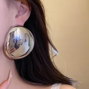Close-up of large oval metallic stud earring in shiny silver finish worn on ear