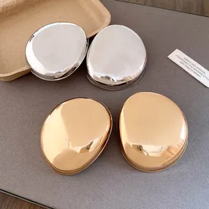 Macro view of polished metal oval stud earrings in gold and silver colored finishes.