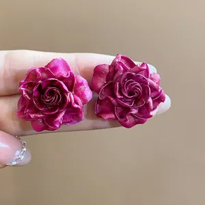 Close-up of magenta resin rose flower stud earrings held between fingers showing realistic scale