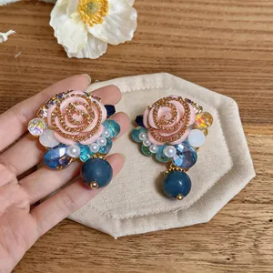 Close-up of vintage resin rose earrings with blue crystal and pearl drop details