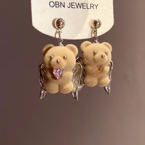 Detailed macro view of cute flocking bear angel earrings with pink heart gem and wings