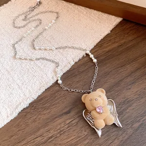 Close-up of cute flocked teddy bear pendant with angel wings and pink heart stone on pearl chain.