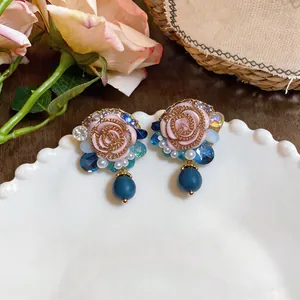 Close-up of vintage French style resin rose earrings with blue crystal accents and beads