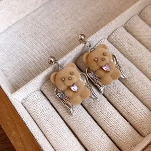 Close-up of flocked teddy bear earrings with angel wings and pink heart zircon.