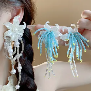 Detailed view of elegant white flower earrings with blue and pearl beaded tassels.
