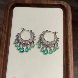 Close-up detail of silver hoop earrings with purple and emerald green zircon teardrop tassels.