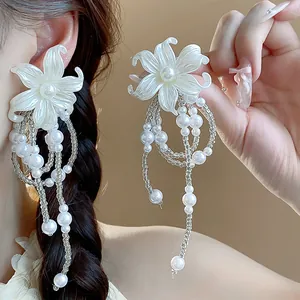 Detailed macro shot of white flower earrings with pearl tassels shown on a model