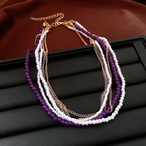 Dettaglio ravvicinato di collana multistrato con perle bianche, perline viola e catene