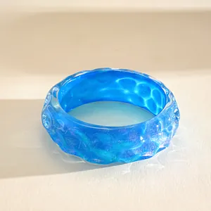Close-up of vibrant iridescent blue resin bangle with wrinkled texture and ocean wave pattern
