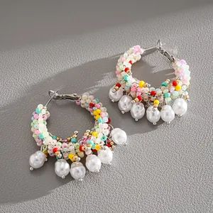 Detailed view of colorful beaded hoop earrings with white pearl pendants on grey surface