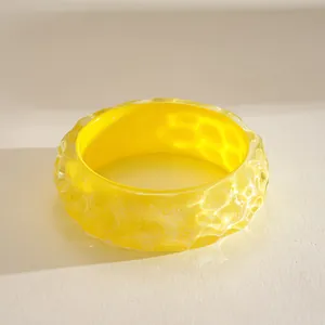 Close-up of a vibrant yellow resin bangle with unique wavy rippled texture