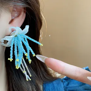 Close-up detail of a white flower earring with light blue beaded tassels on ear