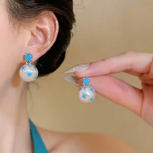 Elegantes pendientes de plata con patrones de estrellas azules mostrados puestos y en mano