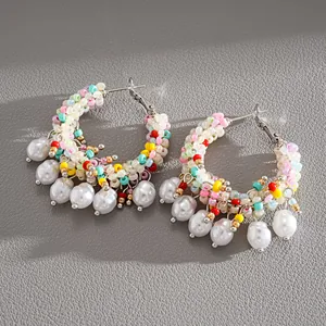 Detailed shot of colorful beaded hoop earrings with pearl charms on grey leather.