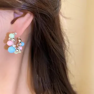 Close-up of a silver hoop earring with colorful beads and sparkling diamonds on an ear