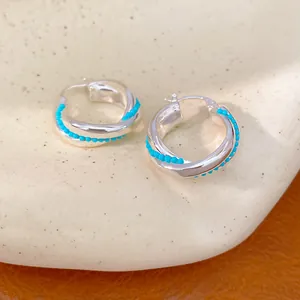 Detailed view of entwined silver hoop earrings with vibrant turquoise blue bead accents