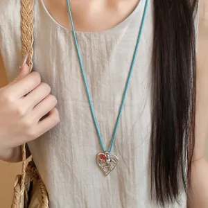 Dettaglio ravvicinato di una collana con ciondolo a cuore traforato e cordino intrecciato blu