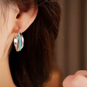 Close-up detail of stylish silver oval hollow earrings featuring vibrant turquoise beads