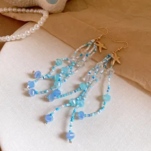 Macro view of blue crystal and bead tassel earrings featuring golden starfish charms for vacation.