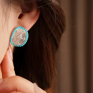 Close-up view of elegant oval hollow earrings with turquoise beads and sparkling zircon