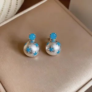 Primer plano de elegantes pendientes de bola de plata mate con estrellas azules y circonita