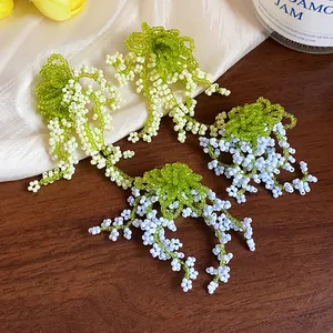 Close-up of handmade green and white glass beaded floral fringe drop earrings