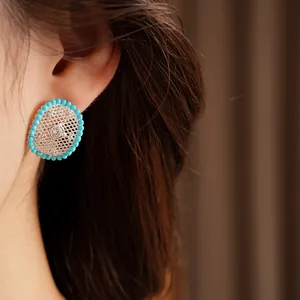 Detail of an oval hollow earring with turquoise beads and zircons on a model's ear