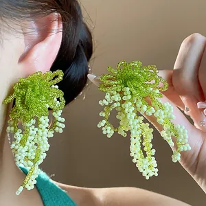 Close-up detail of French pastoral style green glass beaded tassel dangle earrings worn by model