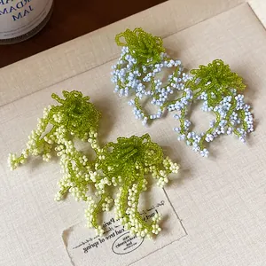 Close-up detail of handmade green and blue glass beaded tassel earrings in forest style