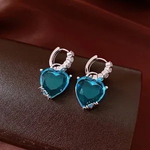 Elegant silver-toned huggie hoop earrings featuring large blue heart-shaped zircons