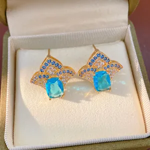 Detailed view of gold-toned earrings with blue and clear zircon stones in a jewelry box