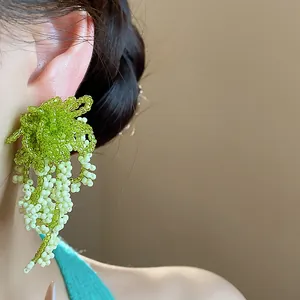 Detailed view of green and white glass beaded tassel earrings worn on a model's ear